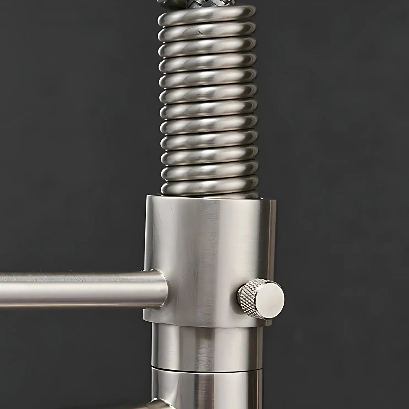 Close-up of a stainless steel kitchen faucet with coiled hose on a dark background