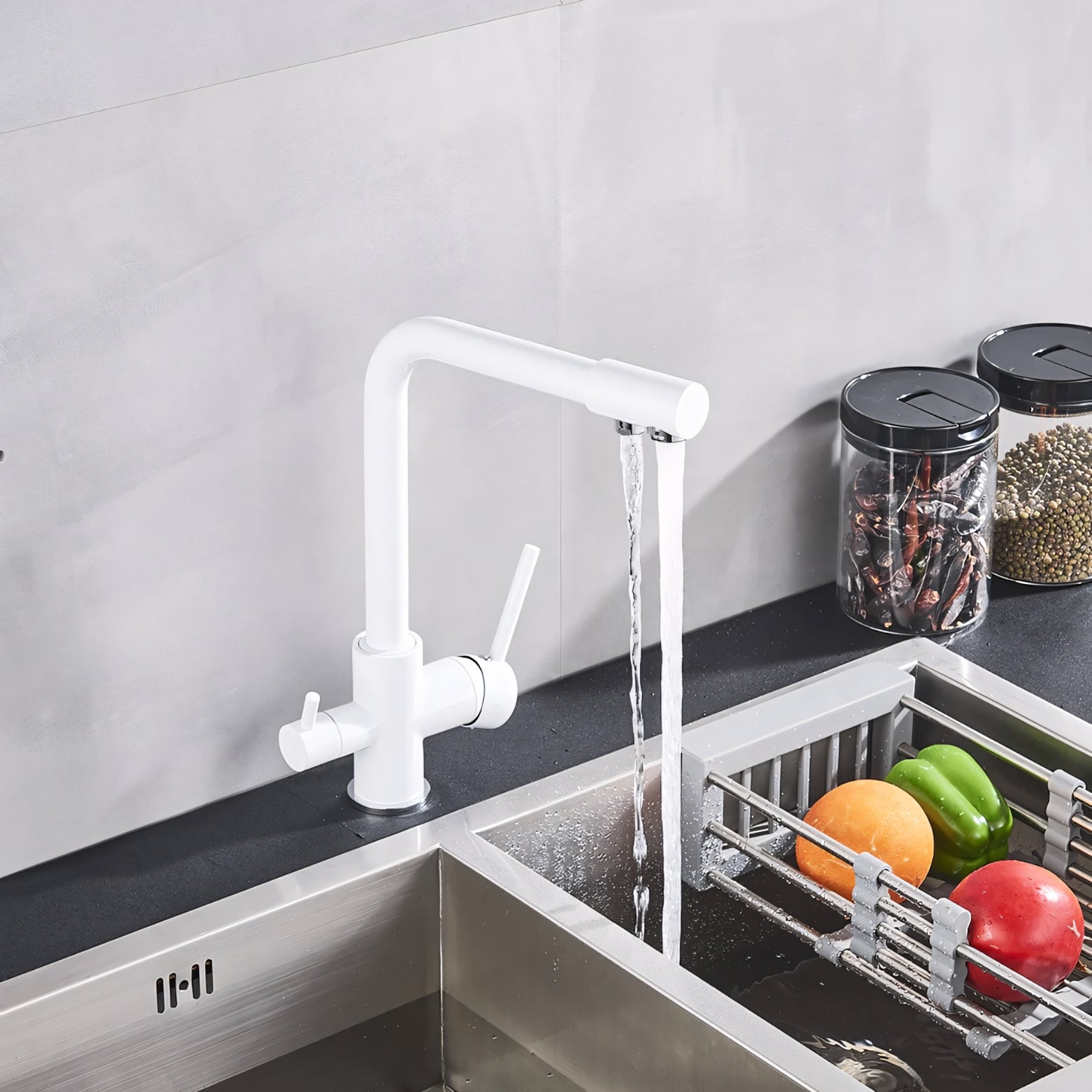 White kitchen faucet with running water over a sink, fruits and vegetables on a rack.