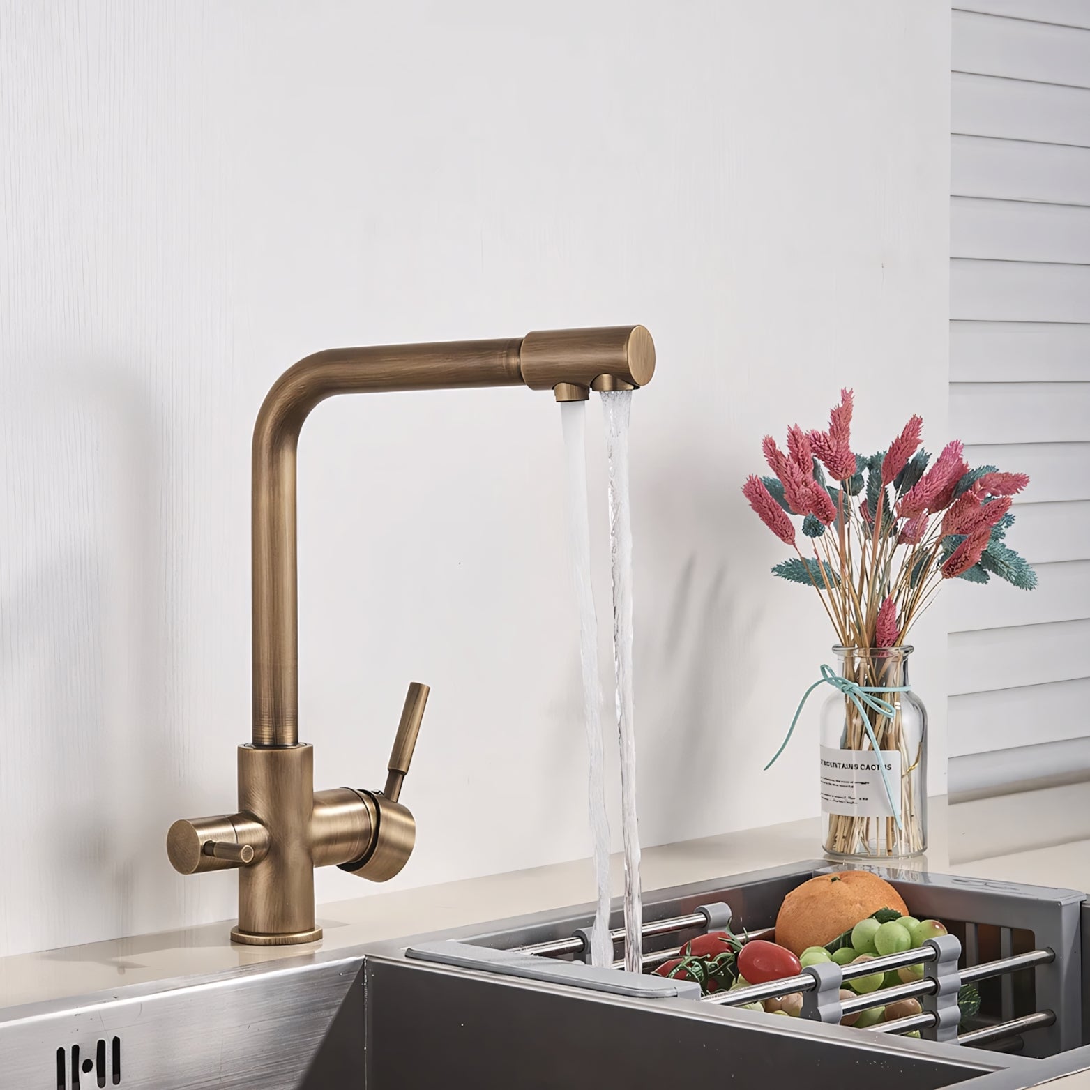 Bronze kitchen faucet with running water in a sink, with a vase of flowers in the background.